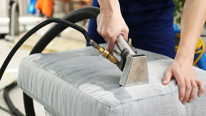 Professional technician cleaning couch upholstery with commercial equipment in San Diego